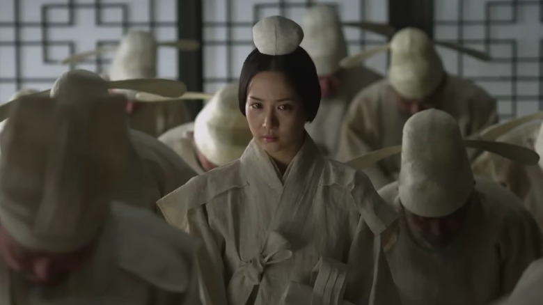 Hwa-yeon standing among various men bowing down in a room in The Concubine (2012)