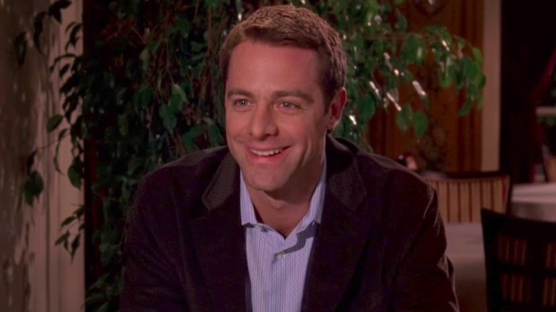 Christopher leaning forward in a chair and smiling on Gilmore Girls