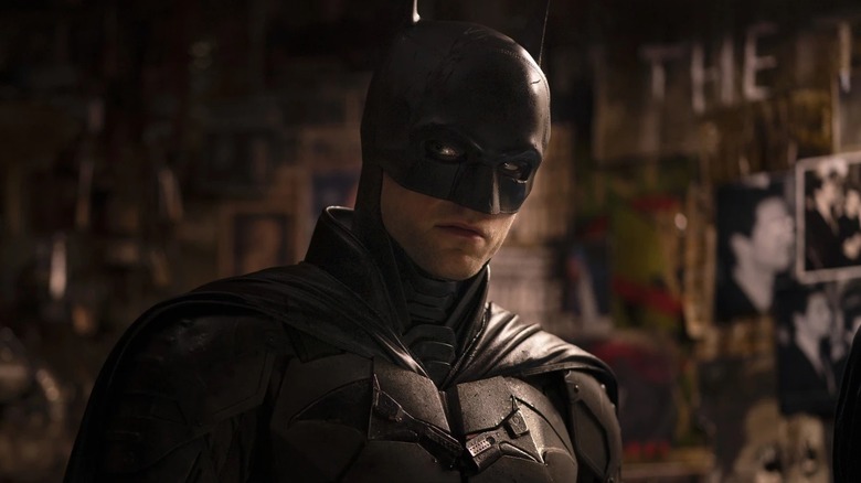 Batman standing next to a wall of pictures in 