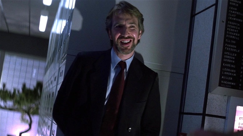 Hans Gruber smiling with back up against a wall in Die Hard