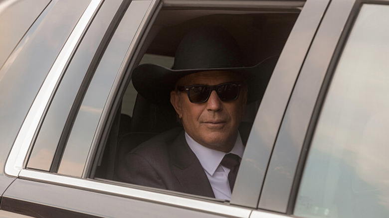 John Dutton looking out of the car window wearing a cowboy hat and sunglasses