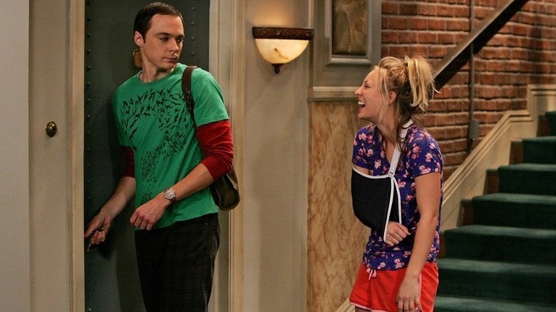 Penny laughing with her arm in a sling and Sheldon entering her apartment on The Big Bang Theory