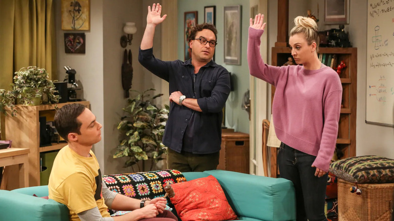 Leonard and Penny raising their hands at Sheldon on the couch on The Big Bang Theory