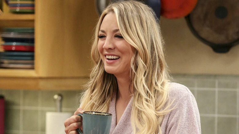 Penny holding a cup of coffee and laughing on The Big Bang Theory