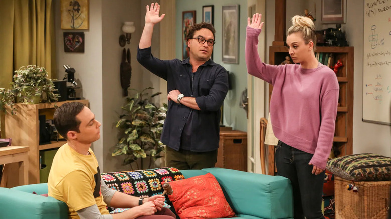 Leonard and Penny raising their hands at Sheldon on the couch on The Big Bang Theory