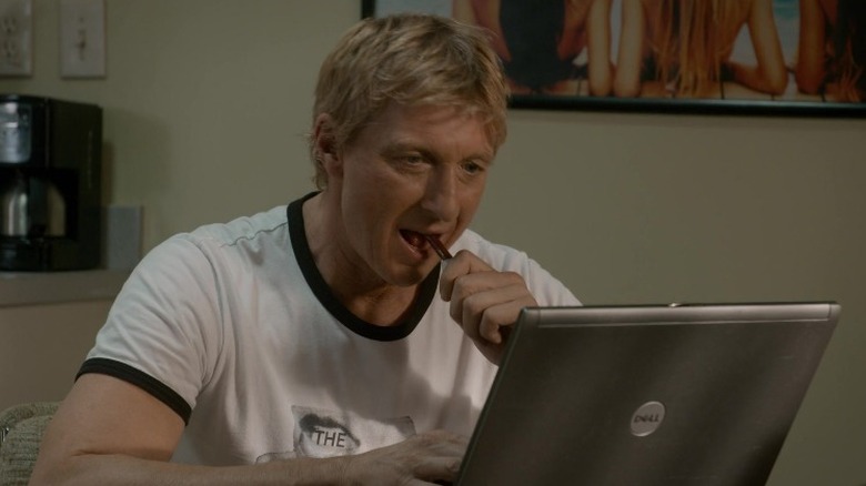 Johnny Lawrence eating a Slim Jim at his computer