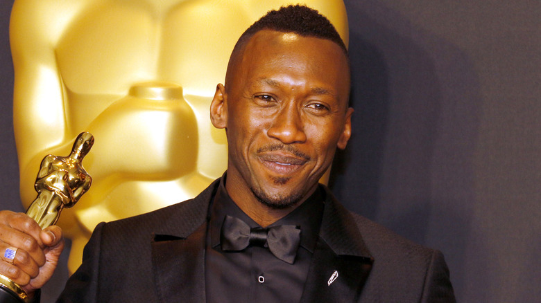 Mahershala Ali holds an Oscar while wearing a black tuxedo