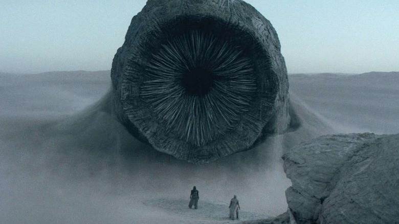 A sandworm confronts two small figures, Paul and Jessica, in "Dune: Part One" (2021)