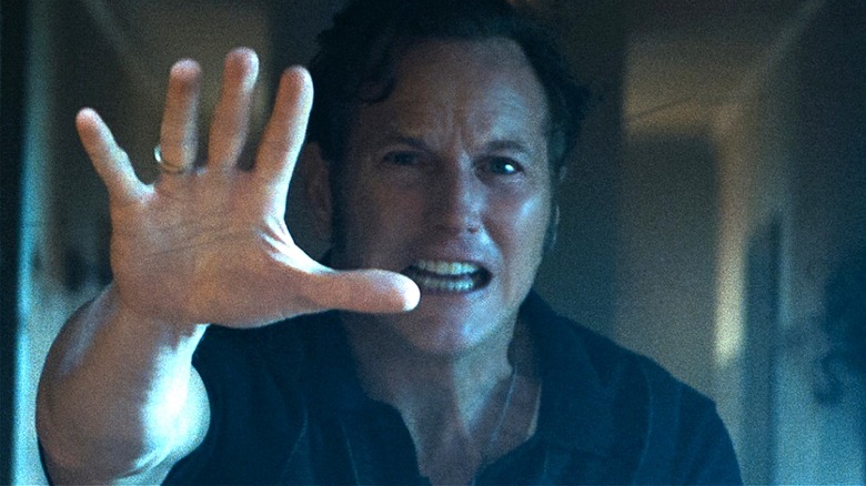 Ed Warren doing an exorcism while Lorraine stands behind him in The Conjuring: Last Rites