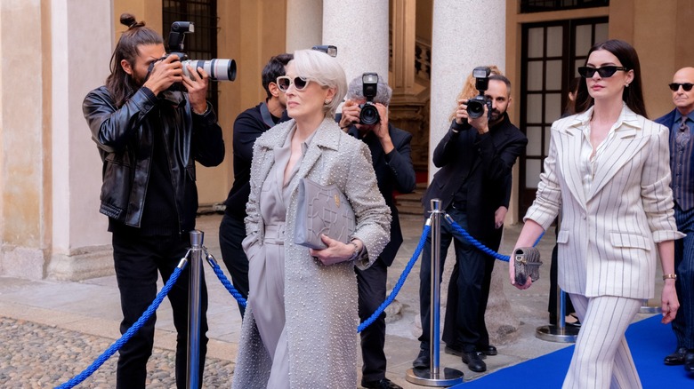 Miranda and Andy walking out of a building in Milan and being photographed in The Devil Wears Prada 2