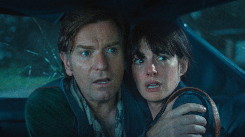 Greg and Denise hide in a car from a dinosaur in The End of Oak Street (2026)