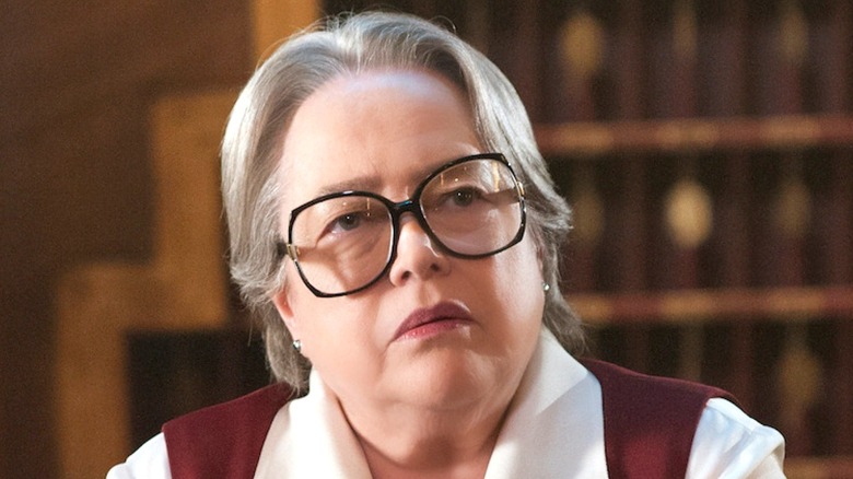 Kathy Bates in glasses behind the check-in desk at Hotel Cortez