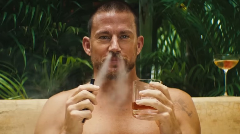 Slater holds a drink and smokes in "Blink Twice" (2024)