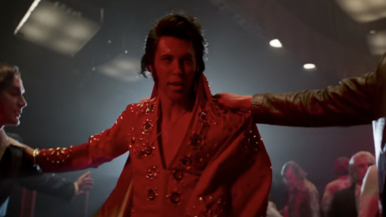 Elvis bathed in red light as an arm on his shoulder leads him away from a crowd