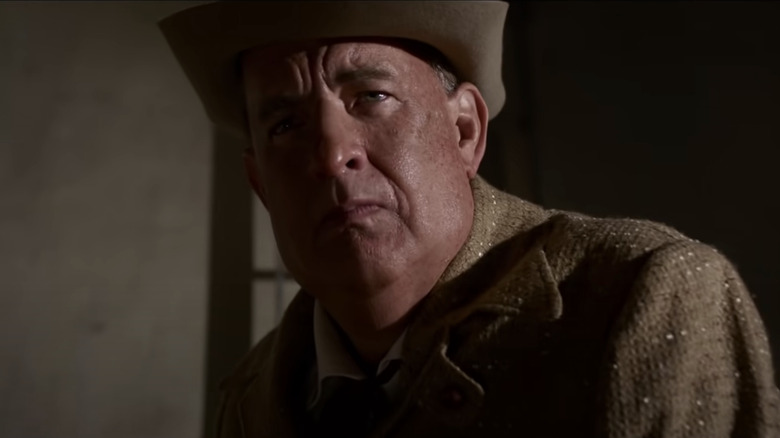 Tom Hanks as Colonel Tom Parker, standing in shadows