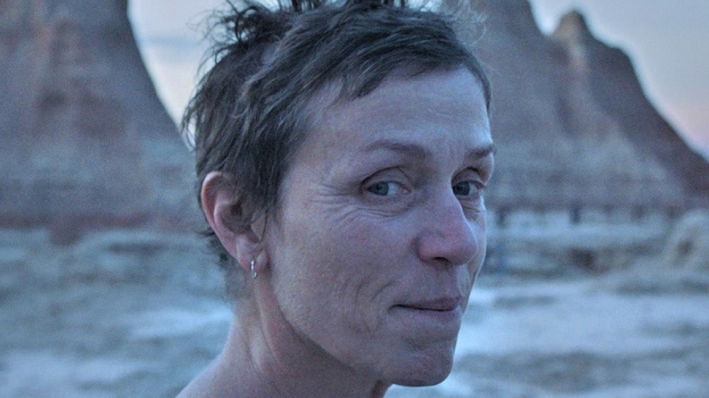 Frances McDormand stands in front of mountains in Nomadland