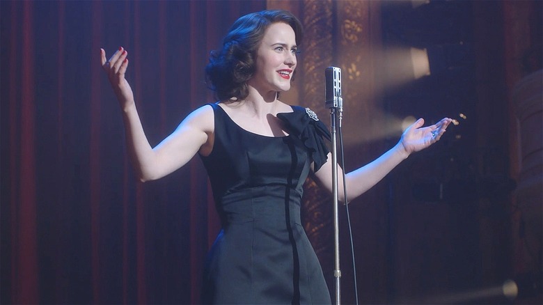 Midge doing stand-up in a black dress