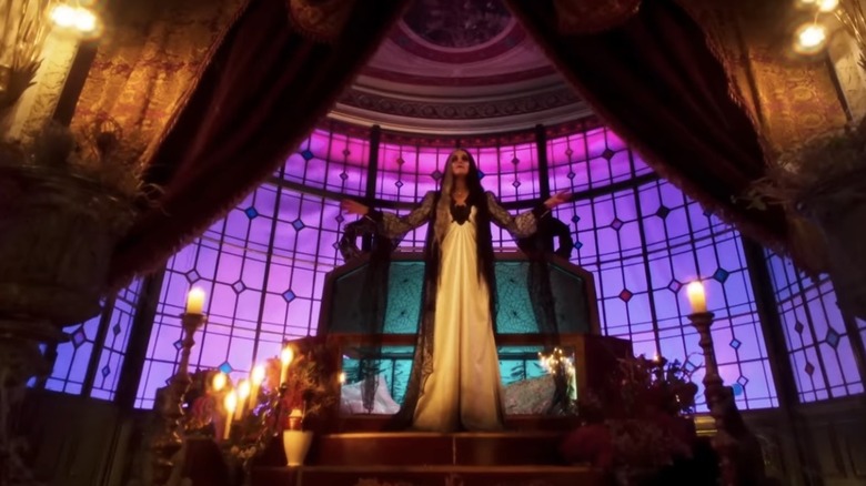 Lily stands in front of an ornate window filled with purple light