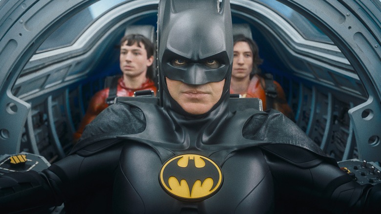 Batman sits in a cockpit with two versions of The Flash behind him