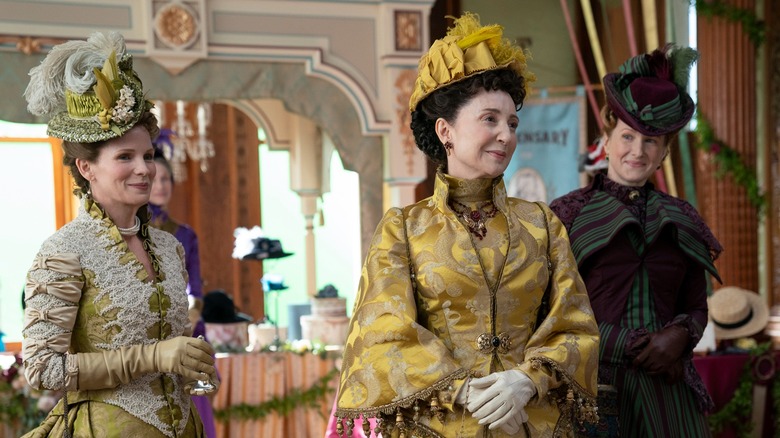 Three women stand in elegant period dress