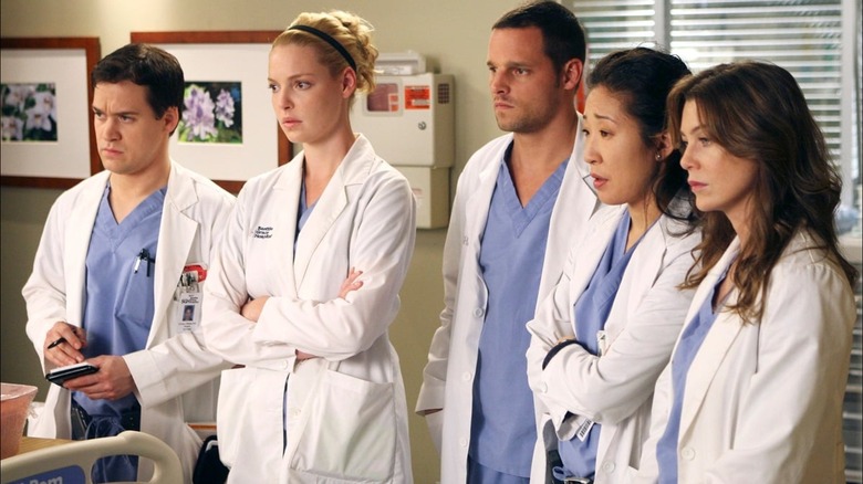 George Izzie Alex Cristina and Meredith in white coats looking at a patient on Grey's Anatomy