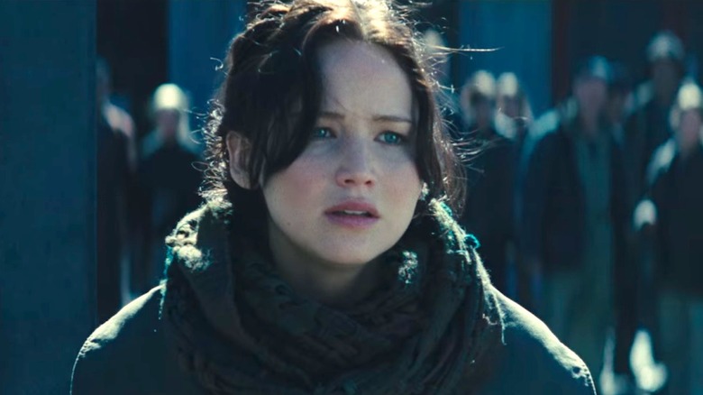 Katniss stands in gray scarf and jacket 