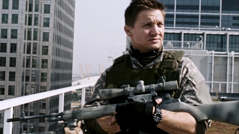 Doyle stands on a rooftop holding a rifle in 