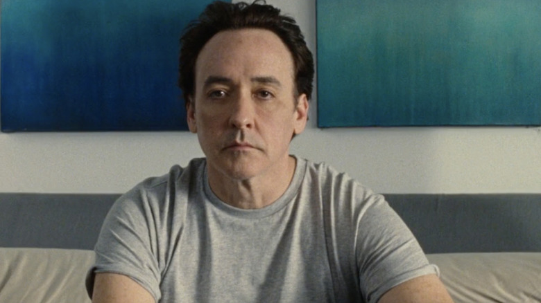 John Cusack sits on bed