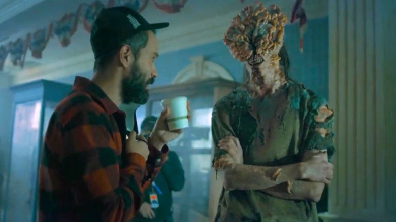 A stunt person with clicker prosthetics being offered coffee behind the scenes while making The Last of Us