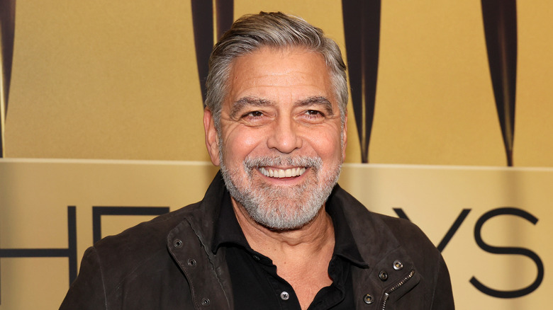 Clooney smiling in front of a poster