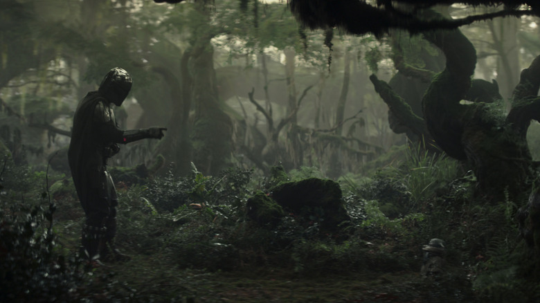 Din Djarin pointing toward Grogu in a forest in The Mandalorian and Grogu