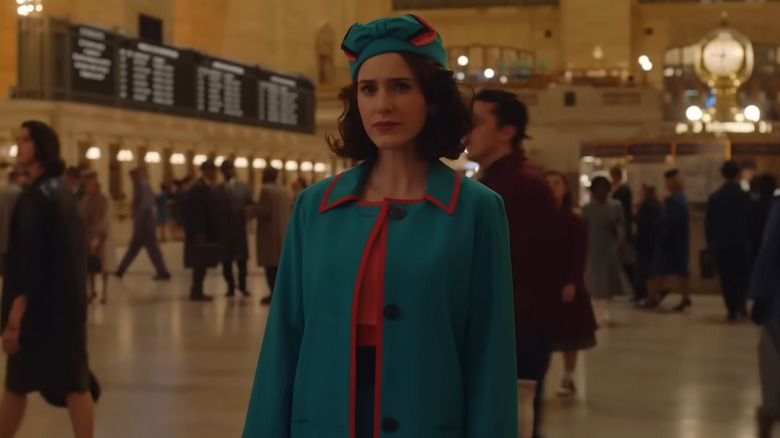 Midge wearing a pink and blue coat standing in Grand Central Station