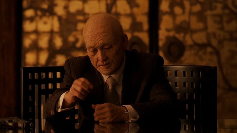 Old Saito siting at desk and playing with totem