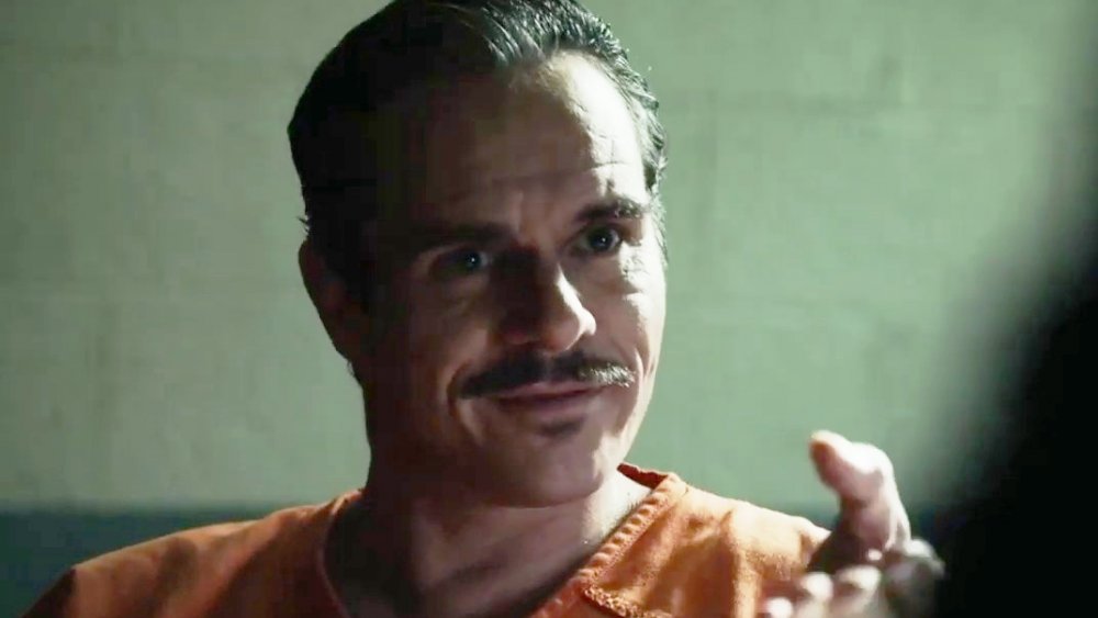 Tony Dalton as Lalo wears an orange prison uniform as he smiles and gestures towards someone off screen on Better Call Saul