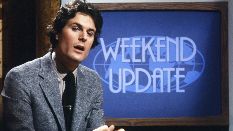Charles Rocket sitting in front of Weekend Update sign (1980)