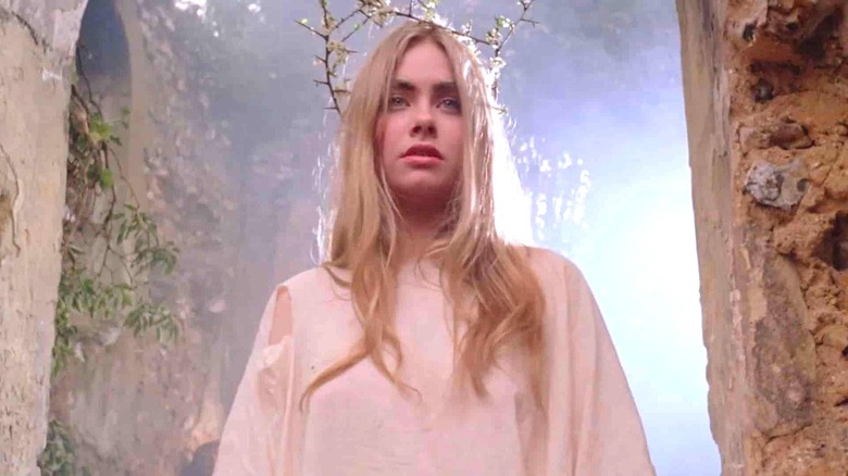 A blonde woman dressed in white is illuminated by an eerie light in a folk horror film