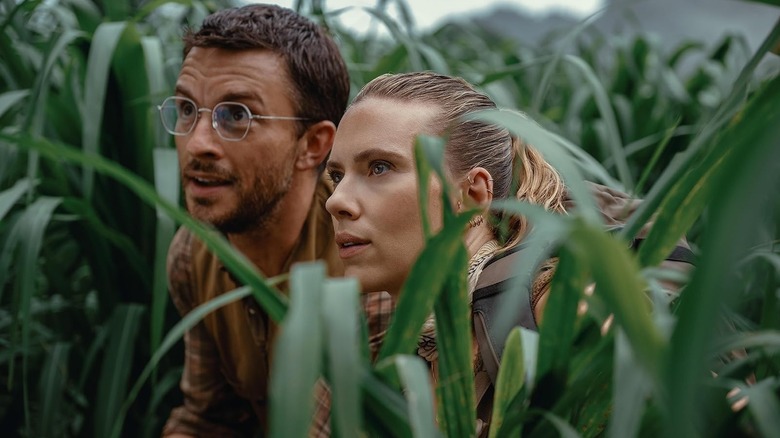 Zora Bennett and Dr. Henry Loomis peering through the bushes in Jurassic World Rebirth