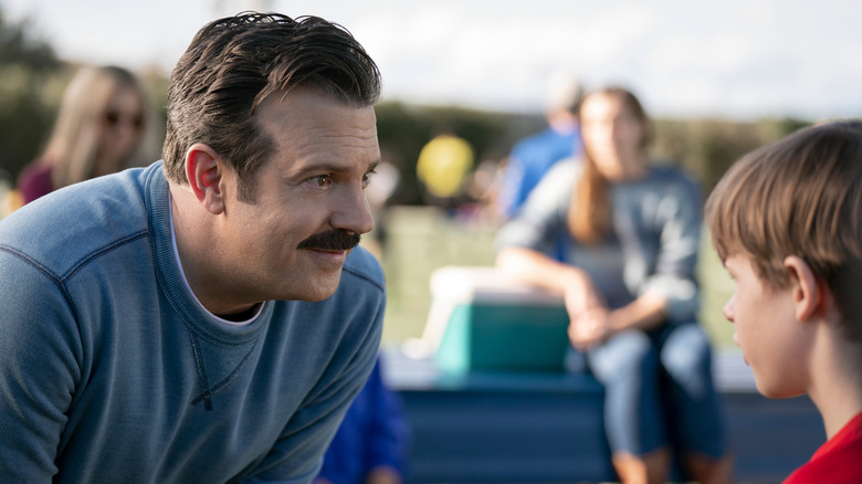 Ted leaning down to coach Henry at a soccer game in Ted Lasso season 3 (2023)