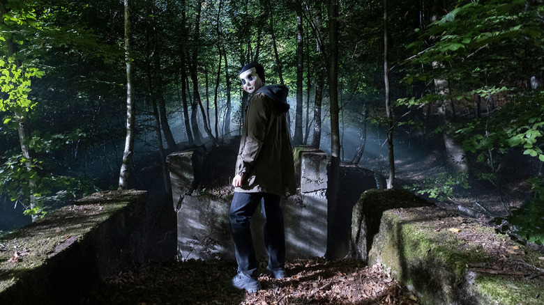 Killer standing in woods looking back in 