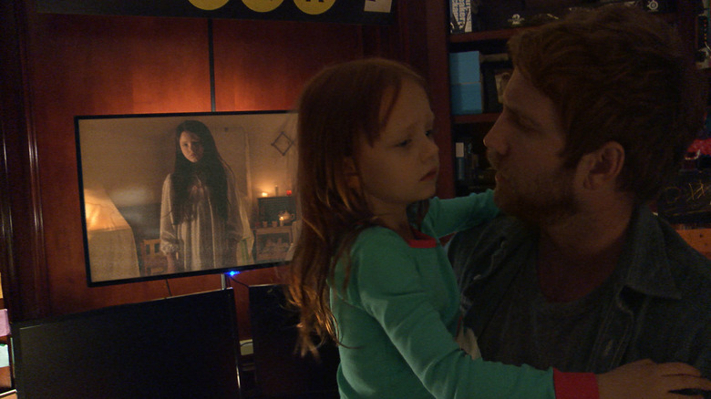 Leila (Ivy George) och hennes pappa (Chris Murray) interagerar med en video av Kristi (Jessica Tyler Brown)