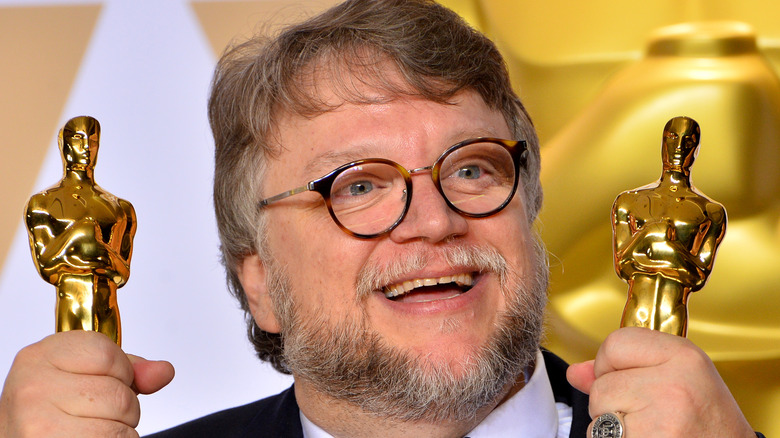 Guillermo del Toro holding two Oscars and smiling