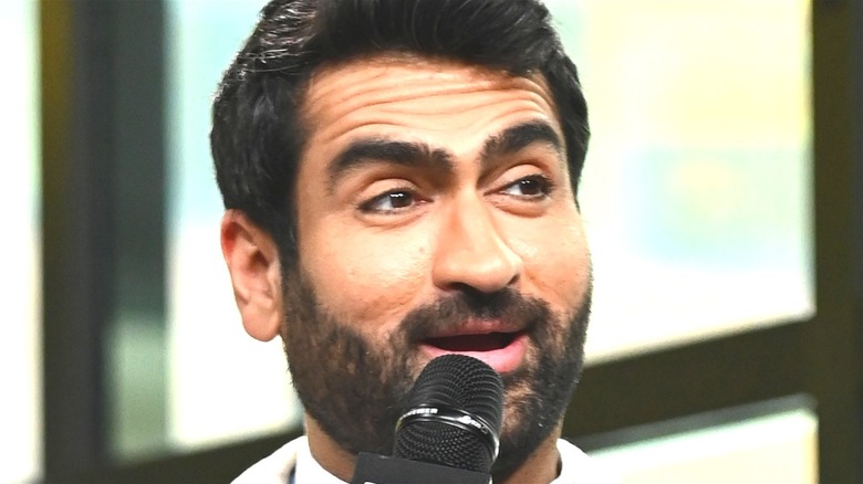 Kumail Nanjiani holds a microphone