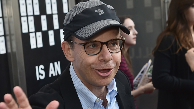 Rick Moranis in a cap and suit waving at an event in 2017