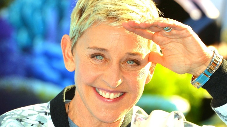 Ellen DeGeneres smiling and blocking sun with hand