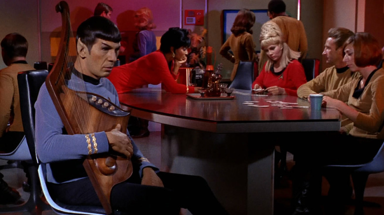 Spock holding a musical instrument as his crewmates play card in "Star Trek"