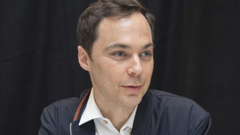 Jim Parsons facing right in front of black curtain