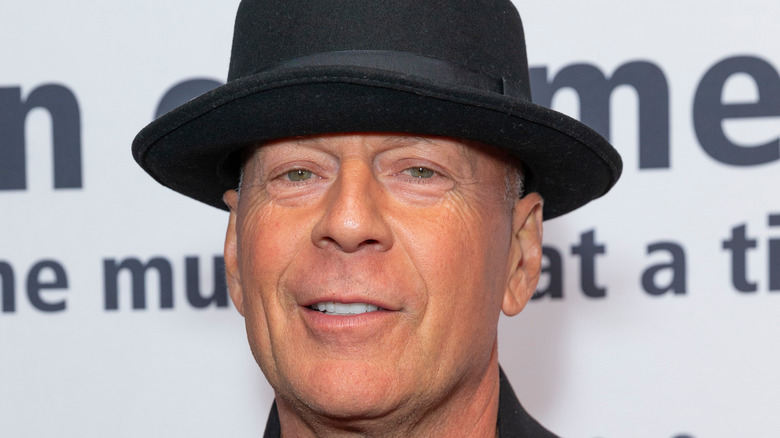 Bruce Willis smiling in black hat