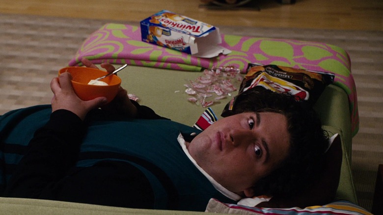 Teenage Ben laying on a snack wrapper-covered couch while eating a bowl of ice cream