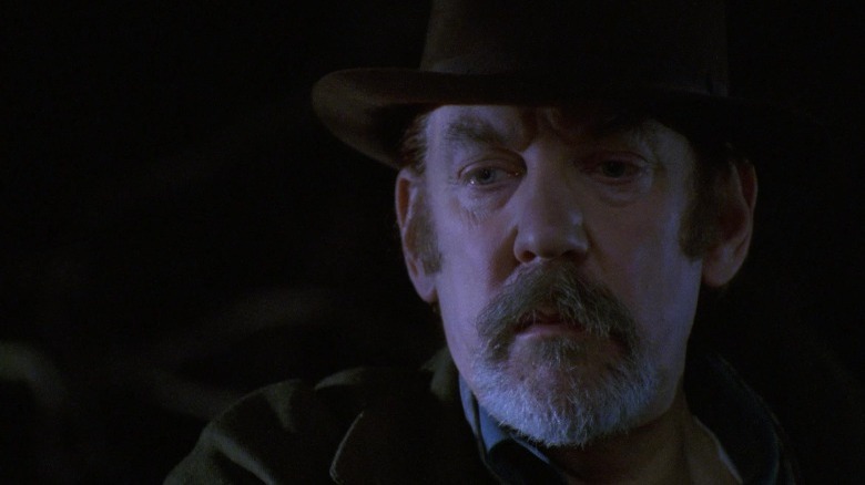 Merrick wearing a fedora and trench coat