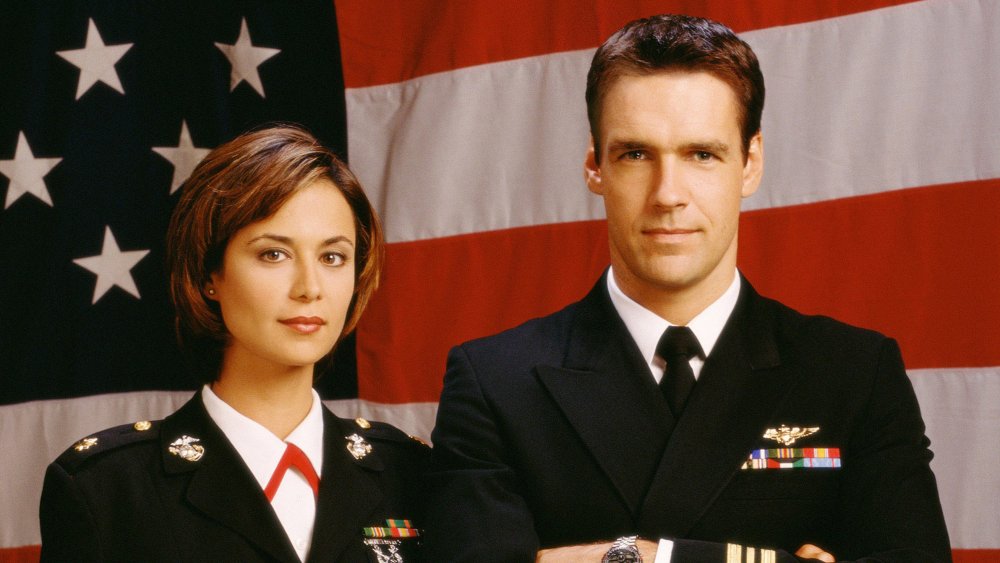 Catherine Bell as Sarah 'Mac' Mackenzie and David James Elliot as Harmon 'Harm' Rabb Jr. stand in front of the Stars and Stripes in uniform in JAG